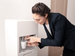 Woman using an office bottleless water cooler to fill a cup