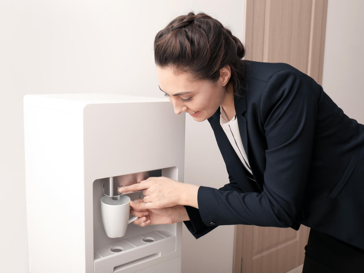 Woman using an office bottleless water cooler to fill a cup